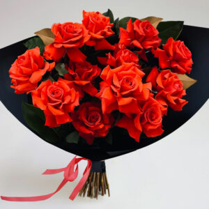 A bouquet of vibrant red roses and green leaves wrapped in black paper with a red ribbon, set against a plain white background, from the Dozen Roses - Wrapped collection.